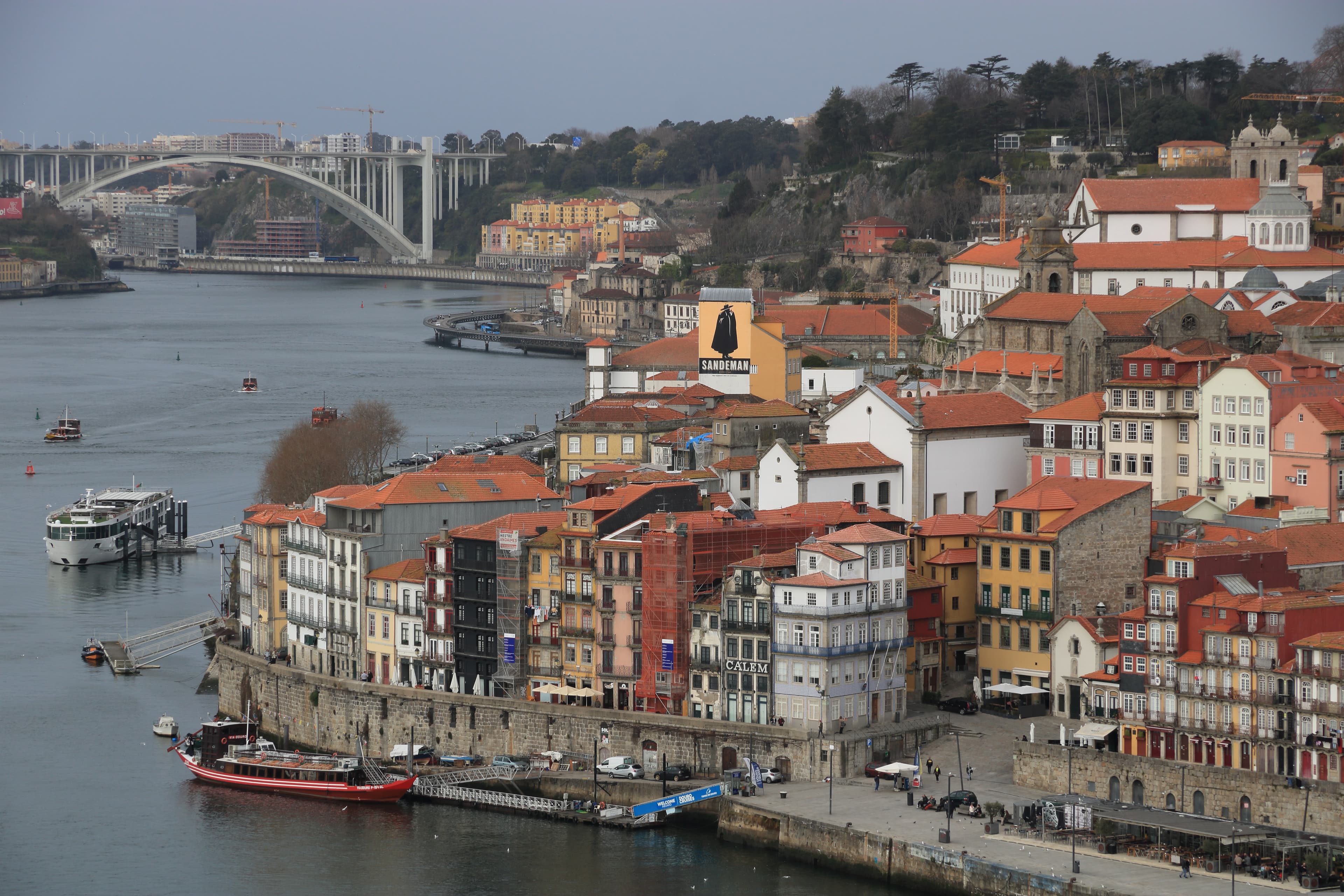 Colorful buildings with terracotta roofs line the Douro River in Porto, Portugal, with boats nearby.