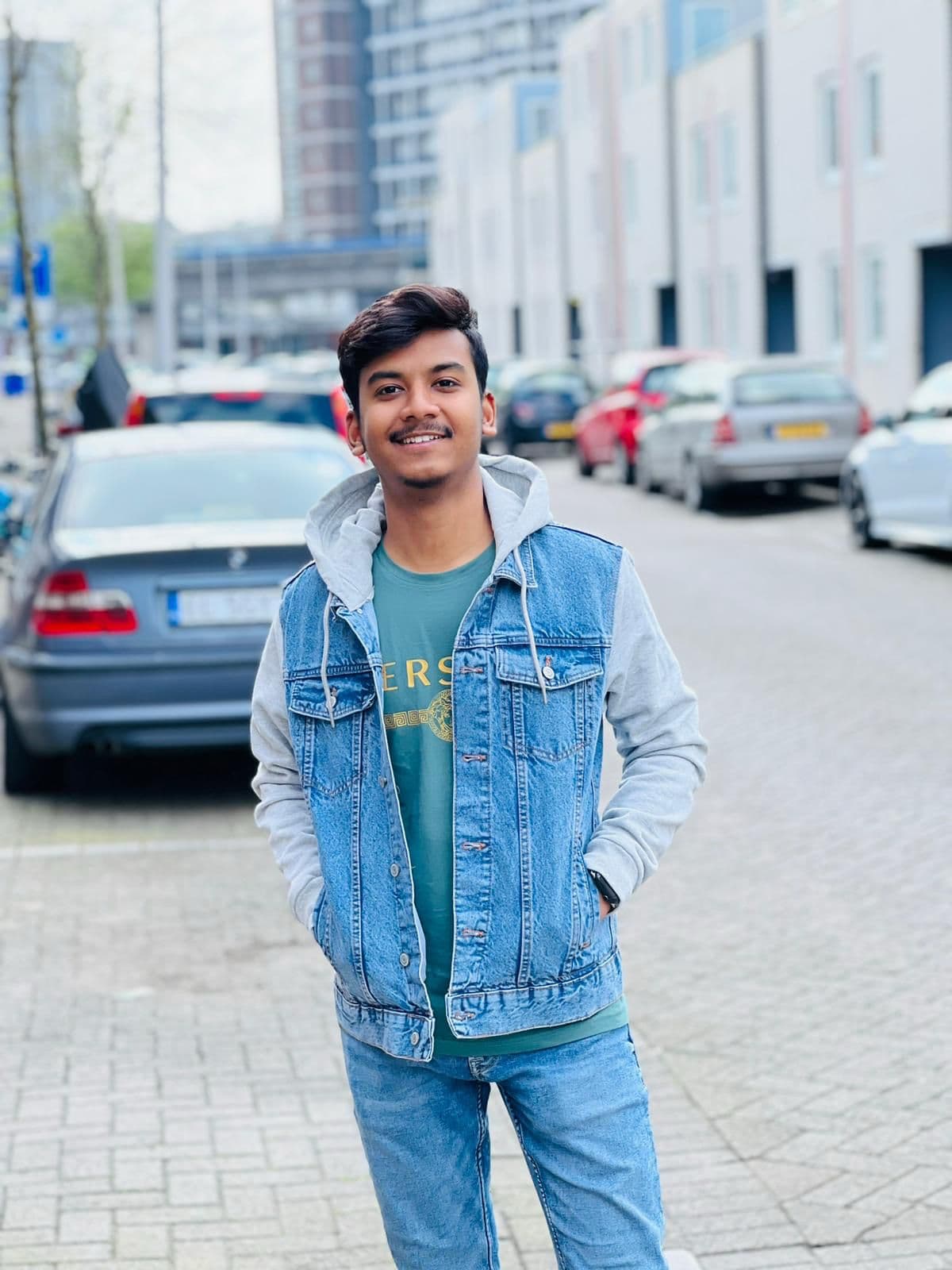 Smiling young man wearing a denim jacket and jeans standing on a city street.